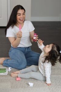 A therapist and a toddler laughing while blowing bubbles during a play-based session